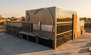 A modern building shaped like a guitar, with a metal facade and glass windows, at sunset.