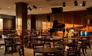 A jazz club with a grand piano, drum set, and bongo drums, surrounded by tables and chairs.