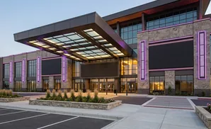 Modern building with large screens and purple lights on a stone facade.