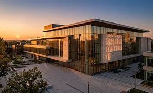 A modern glass and stone building reflects the sunset.