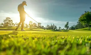 A golfer swings a club towards a ball on a sunny golf course.