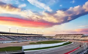 Sunset over a racetrack with grandstands full of spectators and cars lined up.