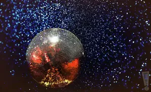 A disco ball reflects red and gold light against a dark background with blue glitter.