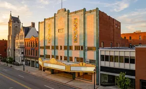 Art Deco theater facade with pastel tiles and neon marquee, flanked by historic buildings and a church.