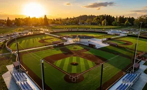 Aerial view of baseball fields at sunset, with stadium seating and a central building.
