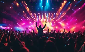 A silhouetted crowd cheers at a concert with vibrant pink and blue stage lights.