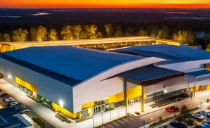 An aerial view of a modern building with a blue roof and yellow accents at sunset.