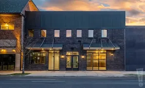 Modern brick building with large glass storefronts and awnings, under a dramatic sunset sky.