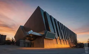 Modern angular building with a large screen, lit by warm sunset light.