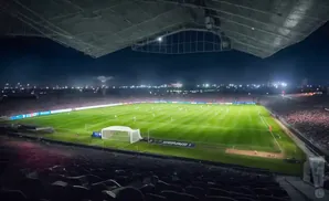 Nighttime view of a well-lit soccer stadium with players on the field and a large crowd in the stands.