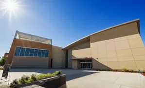 Modern tan building with a large glass entrance and a bright sun in a clear blue sky.