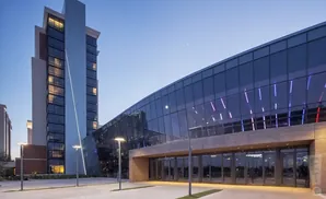 Modern hotel with a tall tower and a curved glass facade illuminated with blue and purple lights.