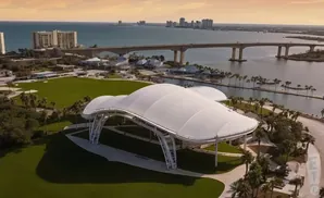 Aerial view of a white-tented amphitheater with a scenic waterfront, bridge, and city skyline in the background.
