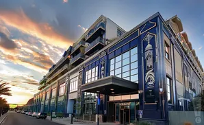 A modern building with blue tiled facade and balconies against a dramatic sunset sky.