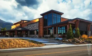 Modern lodge-style building with wood and stone facade, large windows, and scenic mountain backdrop.