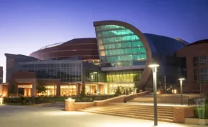 Modern building with curved glass facade at dusk with lit steps and lampposts.