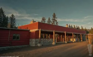 A long, red wooden building with a stone foundation and a covered porch.