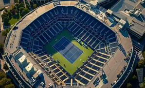 Aerial view of a tennis stadium with a court in the center and empty blue seats surrounding it.