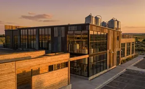 Modern brewery with large windows and silver tanks at sunset.