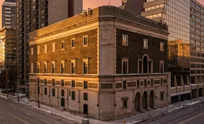 A historic brick building with stone accents stands at a street corner during sunset.