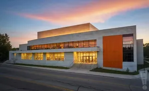 Modern building with stone facade and large windows, illuminated at dusk.