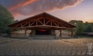 Outdoor amphitheater with rows of empty seats facing a wooden stage, under a dramatic sunset sky.