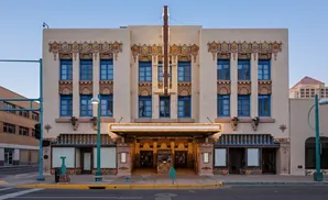 A tan, ornate building with blue windows and a marquee entrance stands under a clear sky.