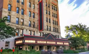 Marquee lights up a historic brick and stone theater building with trees in the foreground.