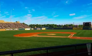 A baseball field with a large crowd in the stands under a blue sky.