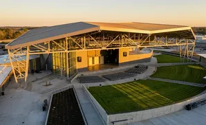 Outdoor amphitheater with a covered stage, tiered seating, and grassy areas at sunset.