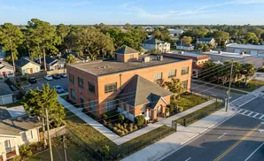 Aerial view of a brick building with an attached smaller building, surrounded by trees, houses, and a street.