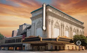 Grand theater entrance with ornate marquee and facade, under a dramatic sunset sky.