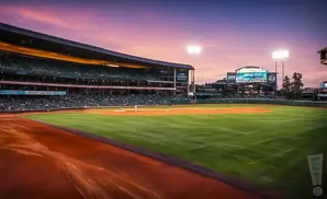 A baseball stadium at sunset, with a batter on the field and lights on.