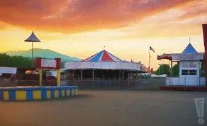 A sunset over a closed amusement park with a carousel and rides.