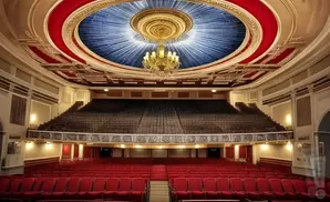 An ornate theater with red seats and a blue, sunburst-patterned ceiling.