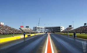 A drag race track with grandstands full of spectators under a clear blue sky.