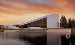 Modern white building with large glass windows reflected in a lake at sunset.