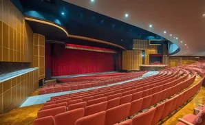 An empty, opulent theater with red velvet seats and a large stage with red curtains.