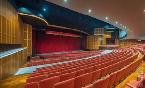 An empty theatre with red seats, a stage with red curtains, and gold paneling on the walls.