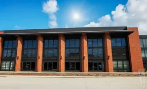 Modern brick building with large windows and glass doors under a blue sky.