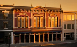 An old red building with ornate details and large windows, flanked by a dark building and a modern tan one.