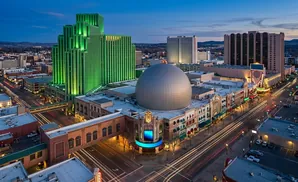 Aerial view of a city skyline at dusk, featuring a prominent green skyscraper and a large domed building.