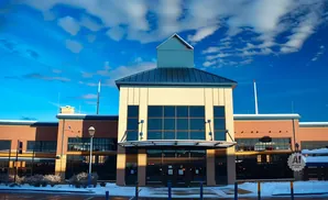 A modern brick and beige building with large windows under a bright blue sky with clouds.
