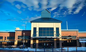 A modern building with a light-colored facade and dark windows, set against a bright blue sky with scattered clouds.