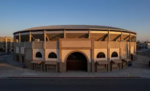 A large, round stadium with tiered seating and a large arched entrance at sunset.