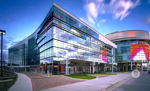 Modern glass building with curved architecture and digital displays, reflecting a cloudy blue sky.