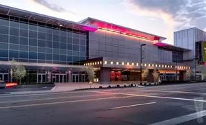 Modern building with large glass windows and pink lighting at dusk, with a street in the foreground.