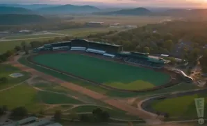 Aerial view of a horse racing track at sunset, with grandstands and surrounding landscape.