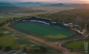 Aerial view of a racetrack with green infield and grandstands, at sunset.