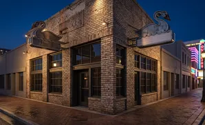 A brick building with swan signs and neon lights at dusk.